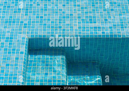 The intricate pattern of small blue tiles forms a textured surface on the steps and walls of a pristine swimming pool Stock Photo