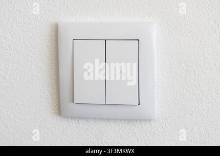 A close-up view of a contemporary white dual rocker switch mounted on a rough textured wall surface Stock Photo