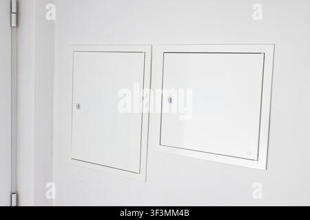 Minimalist interior scene featuring two identical white access panels mounted on a textured white wall, highlighting architectural details Stock Photo