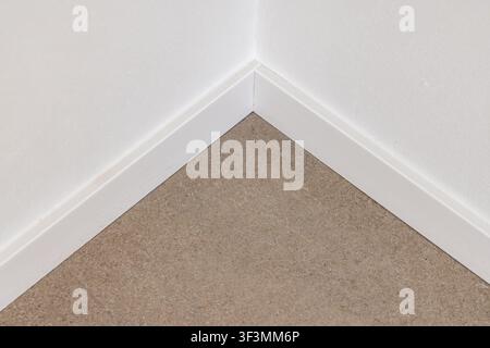 A simple interior corner where a white painted baseboard meets a speckled beige carpeted floor, showcasing architectural detail Stock Photo
