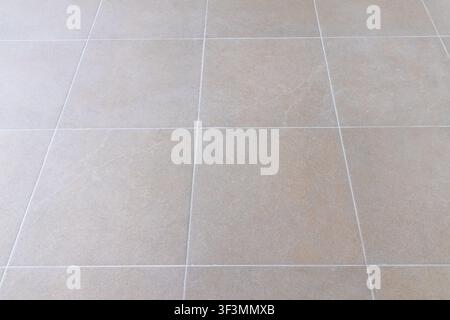 A close-up view of large, square beige tiles laid out in a grid pattern, showcasing their fine-grained texture and the thin white grout separating the Stock Photo