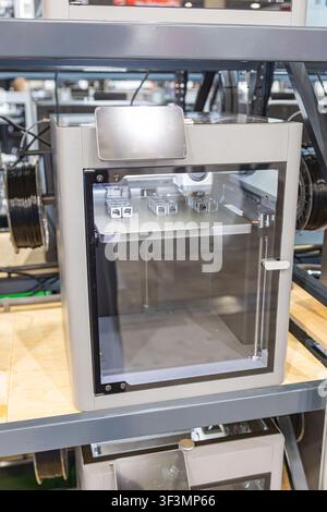 3D printer in industrial workshop, sleek rectangular machine with transparent front panel, metallic finish, control display, printing bed objects, hig Stock Photo