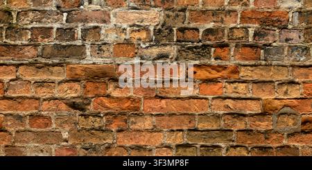 An old, weathered red brick wall with remnants of mortar and plaster patching, displaying a rustic, antique quality. Stock Photo