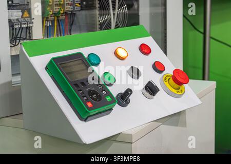 Control panel with digital display, various buttons and knobs, green and red accents, mounted on white surface, bright even lighting, indoor industria Stock Photo
