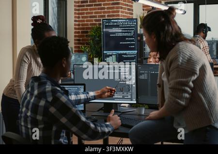 Programmer sits on a desk and discusses artificial intelligence innovation with a mixed team reviewing machine learning algorithms. Stock Photo