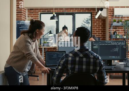 Two software developers doing high five hand gesture at desk with multiple screens running ai code celebrating successful algorithm, programmers colleagues enjoying teamwork results in it agency. Stock Photo
