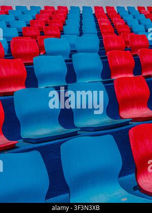 Rows of empty red and blue plastic seats in an outdoor sports stadium. Stock Photo