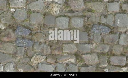 A textured view of uneven antique stone cobblestones with moss and grass growing between the cracks. Stock Photo