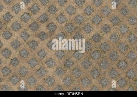 A top-down view of a permeable concrete grid paving system designed for grass, showing square cement blocks with dried yellow grass growing in between Stock Photo