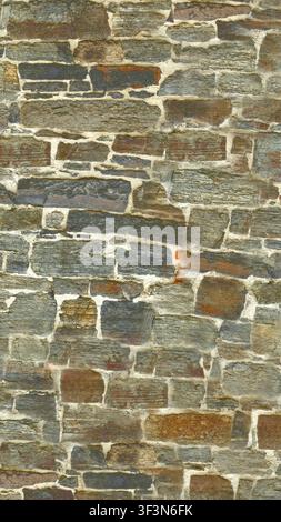 A textured background of a medieval wall featuring varied, multicolored slate stones fitted with mortar. Stock Photo