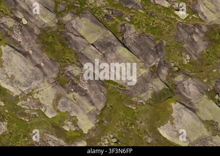 An aerial top-down view of rugged mountain rock terrain covered in patches of green moss and lichen. Stock Photo