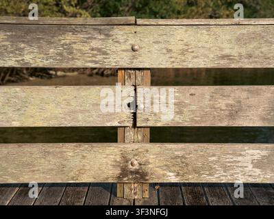 Three thick horizontal wooden planks tightly attached to a vertical wooden support with large metal bolts form a heavy protective wooden railing. Stock Photo