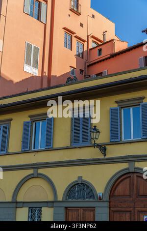 A charming view of historic Italian architecture featuring contrasting yellow and peach facades with traditional shutters, arched doorways, and elegan Stock Photo