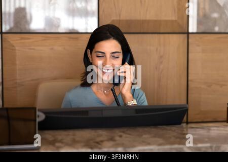 Smiling female receptionist talking on phone at hotel reception desk Stock Photo