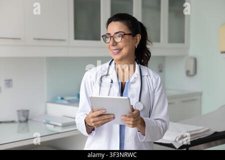 Happy senior practitioner doctor woman in white coat holding tablet Stock Photo