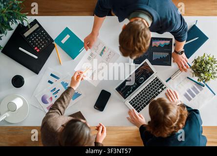 Dynamic top view of a diverse group of business professionals collaborating on a project in a modern workspace. The team is analyzing financial graphs Stock Photo