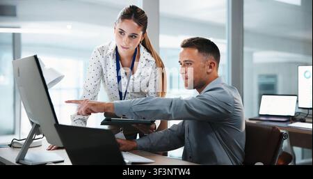 Businessman, pointing and computer with coworker for analytics or performance review in office. Man, woman or showing colleague data with technology Stock Photo