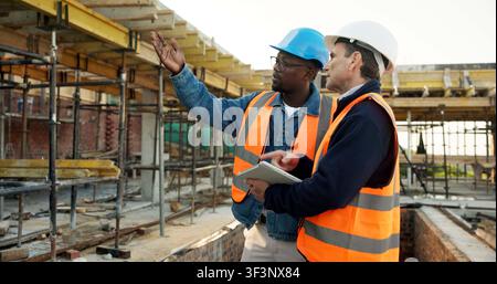 Construction site, team and planning with engineer, tablet and safety inspection for development. Men, tech and talking outdoor for building Stock Photo