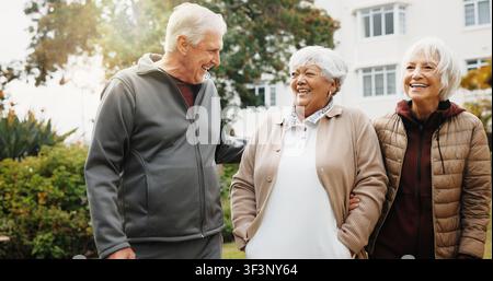 Outdoor, fitness and old people by retirement home with laugh, funny story and walk for exercise. Happy, senior friends and wellness by apartment Stock Photo