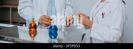 Two Scientists Collaborating Over Colorful Chemical Solutions and Test Tubes in a Modern Laboratory Stock Photo