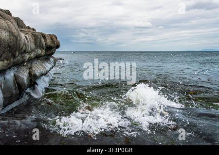 Dynamic coastal scene near Sligo on the Atlantic coast of Ireland. A breaking wave crashes against smooth layered rock formations in the foreground, s Stock Photo