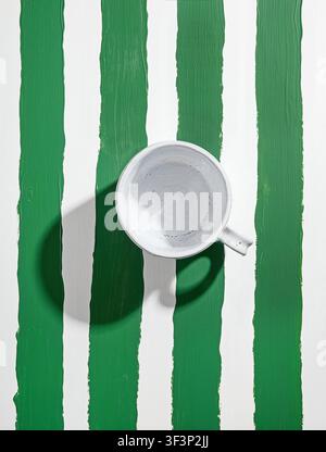 empty white ceramic coffee cup on painted green and white striped table, top view Stock Photo