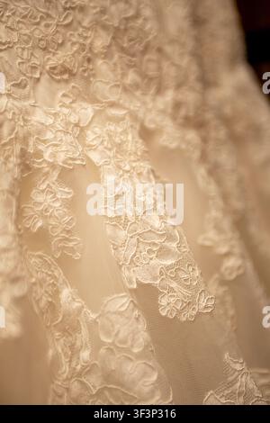 An elegant, soft-focus macro photograph capturing the detailed textures of a bridal dress. The image showcases delicate, multi-layered floral lace app Stock Photo