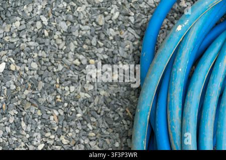 Coiled blue garden hose resting on gray gravel surface with ample copy space ideal for irrigation gardening outdoor maintenance and utility concepts Stock Photo