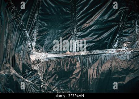 Dark, shiny polyethylene material background showing wrinkled, reflective surfaces and textured vertical lines. with dramatic highlights and creased f Stock Photo