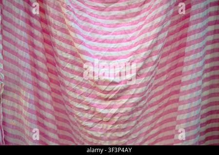 Soft pink and white striped fabric hangs in gentle folds, creating a textured, vintage-inspired backdrop. Wrinkled, cotton-like textile evokes cozy, f Stock Photo