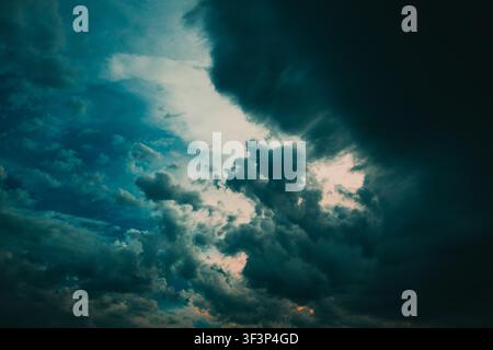 Moody, dramatic storm clouds sweep across a turbulent evening sky, creating strong contrast and a sense of impending weather. Dark, textured clouds an Stock Photo
