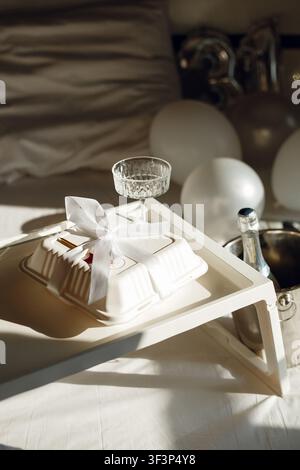 Wrapped and decorated cake with champagne bottle and balloons on tray with sunlight Stock Photo
