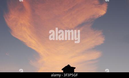 Dramatic Pink Feather Cloud over Roof Silhouette at Sunset Stock Photo