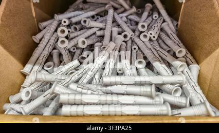 A large quantity of grey plastic wall anchors are piled high inside a brown cardboard box, ready for purchase Stock Photo