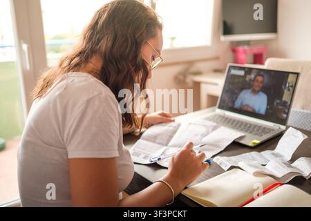 Woman reading documents and taking notes while attending an online video call class Stock Photo