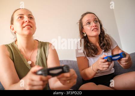 Friends concentrating while playing video games together indoors Stock Photo