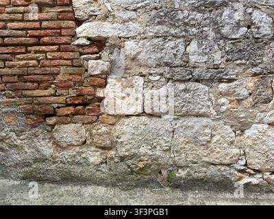 A rustic exterior wall shows a patchwork of exposed old brick and rough-hewn stone repairs, weathered by age and time. Stock Photo