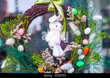 Easter door wreath made of twigs with white plush bunny toy colorful eggs and spring green plants decorations Stock Photo
