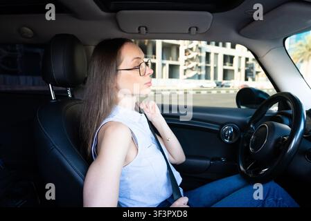 Young woman sitting in a car touching her face during allergy or cold symptoms. Healthcare, illness and seasonal wellness concept. Stock Photo