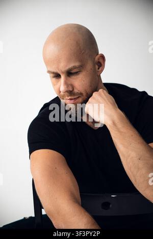 Man with a bald head and beard sits thoughtfully in a studio setting Stock Photo