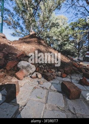 Pile of rocks, bricks, and dirt on a stone walkway under tall trees in a park, showing outdoor damage and rough ground Stock Photo