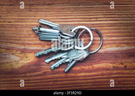 A bunch of metal keys attached to a key ring lie on a textured wooden surface, illustrating everyday access and security concepts with a rustic and vi Stock Photo
