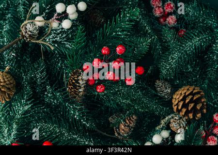 Snowy Christmas tree branches with red berries, frosted white berries and natural pine cones. Christmas and New Year concept. Stock Photo