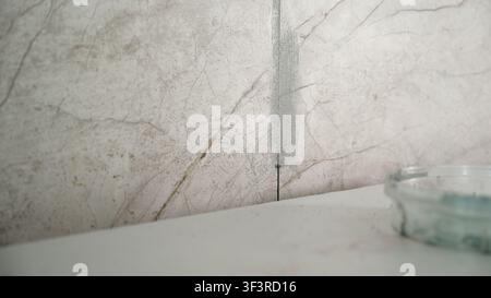 Grout for ceramic tiles in the kitchen. Carefully filling the joints between square ceramic tiles on a kitchen wall with a tool during a home Stock Photo