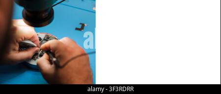 Close-up of hands repairing electronic circuit board with tools on blue work surface, focused on intricate components and connections Stock Photo