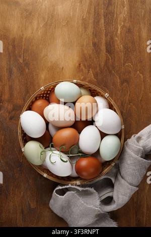 Vertical top view of colorful organic farm eggs in a wicker basket on a rustic wooden table with copy space. Fresh multicolored chicken eggs from eco Stock Photo