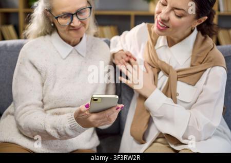 Daughter guides elderly mother using smartphone for online services and tasks Stock Photo