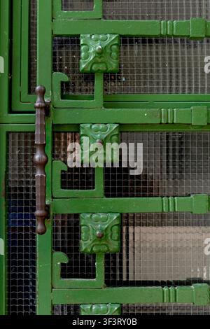 A close-up view of a green painted metal gate with decorative panels and wire mesh. The frame, handle, and textured surface create an abstract archite Stock Photo