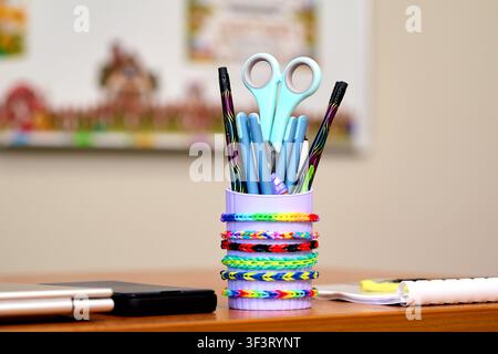 Cute school stationery holder with colorful rainbow loom bands on desk. Stock Photo