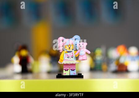 A toy minifigure of a girl with pink and blue ponytails holding a teddy bear. Сonstruction set. Stock Photo